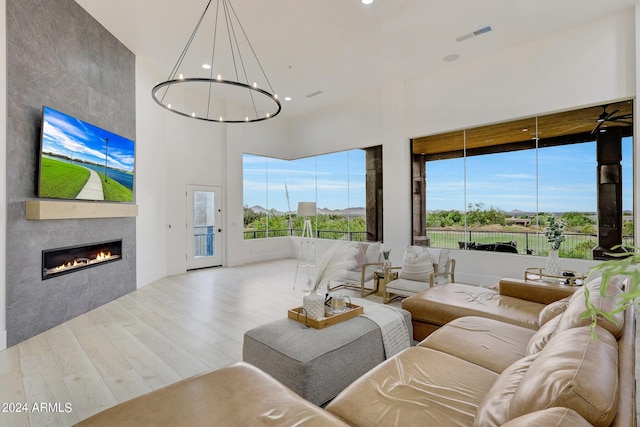 living room with an inviting chandelier, a towering ceiling, light hardwood / wood-style flooring, and a tile fireplace