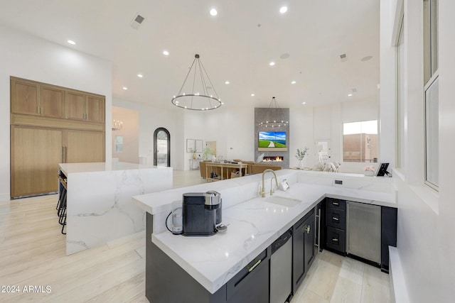 kitchen featuring sink, hanging light fixtures, a spacious island, light stone counters, and light hardwood / wood-style floors