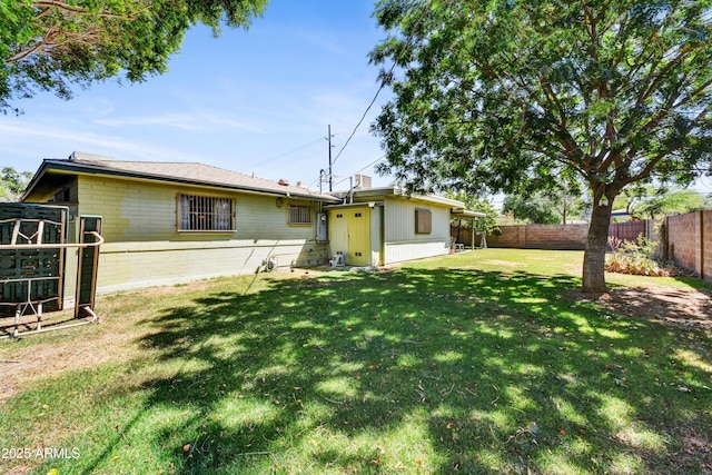 rear view of property featuring a lawn, concrete block siding, and a fenced backyard