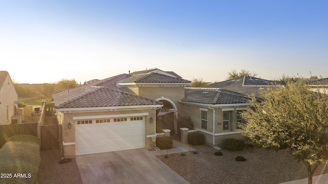 mediterranean / spanish home featuring a garage, a tiled roof, driveway, and stucco siding