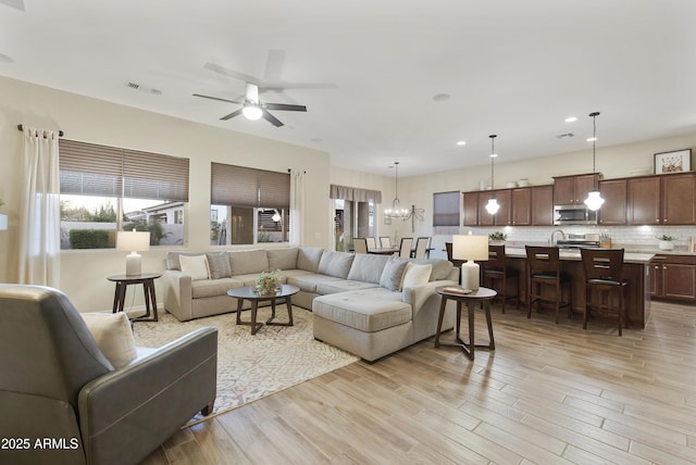 living area featuring ceiling fan with notable chandelier, light wood finished floors, visible vents, and recessed lighting