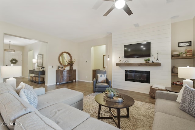 living area with ceiling fan, a fireplace, baseboards, and wood finished floors