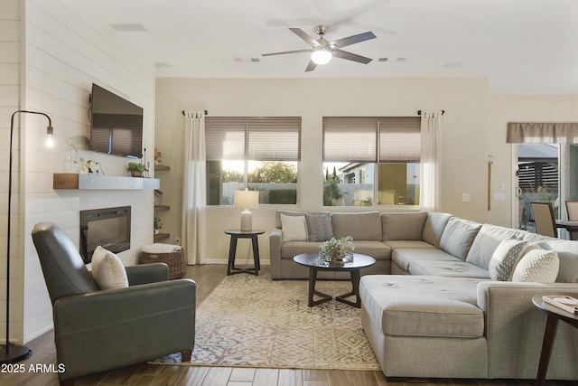 living room with a ceiling fan, wood finished floors, and a glass covered fireplace