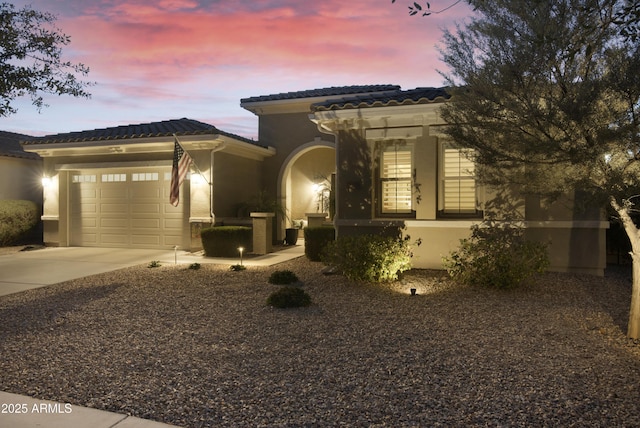 mediterranean / spanish-style house with an attached garage, driveway, a tile roof, and stucco siding