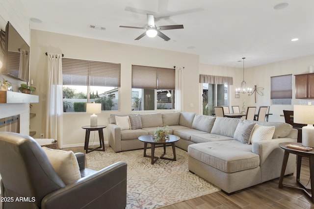 living room with ceiling fan with notable chandelier, a glass covered fireplace, visible vents, and wood finished floors