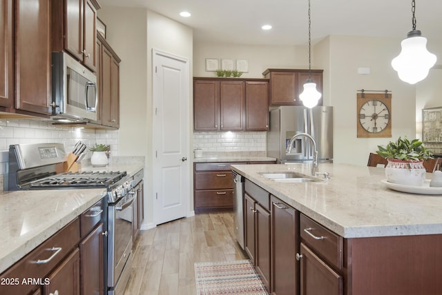 kitchen with stainless steel appliances, a sink, light stone countertops, and pendant lighting