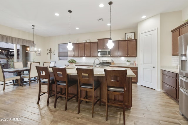 kitchen featuring wood finish floors, a kitchen breakfast bar, appliances with stainless steel finishes, backsplash, and a center island with sink