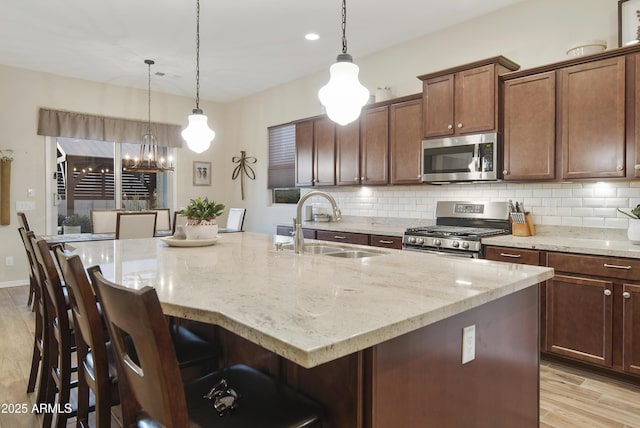 kitchen featuring appliances with stainless steel finishes, a sink, light wood-style flooring, and decorative backsplash