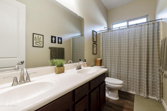 full bath with double vanity, a sink, toilet, and wood finished floors