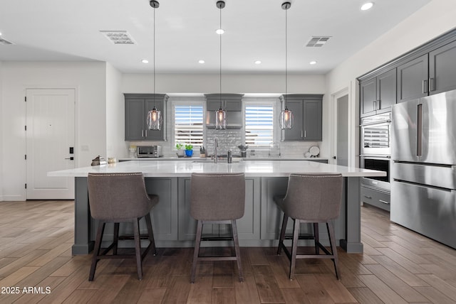 17385 W Sugar Hill Ct, Surprise, AZ 85388 - kitchen with stainless steel appliances, a sink, gray cabinets, decorative backsplash, and an island with sink