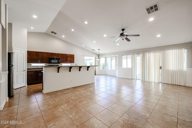 kitchen featuring light tile patterned floors, stainless steel fridge, ceiling fan, a kitchen bar, and a center island with sink