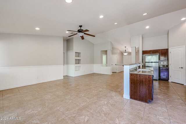 kitchen with an island with sink, stainless steel refrigerator, sink, ceiling fan, and light stone counters