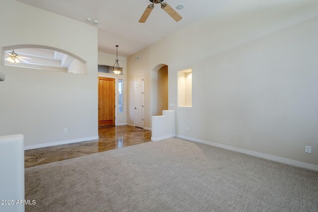 spare room featuring carpet flooring, a ceiling fan, arched walkways, and baseboards