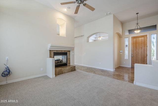 unfurnished living room with arched walkways, carpet, a ceiling fan, baseboards, and a tile fireplace