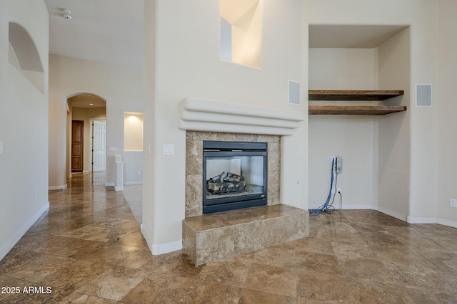 unfurnished living room with arched walkways, baseboards, visible vents, and stone finish floor