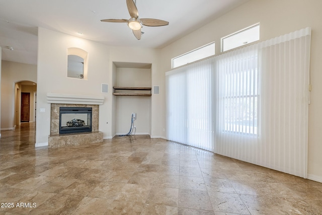 unfurnished living room featuring a tiled fireplace, arched walkways, baseboards, and a ceiling fan