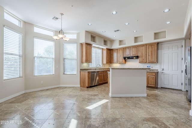 kitchen with appliances with stainless steel finishes, an inviting chandelier, a center island, stone tile floors, and baseboards