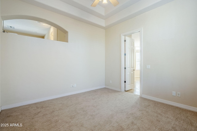 spare room featuring a ceiling fan, a tray ceiling, light colored carpet, and baseboards