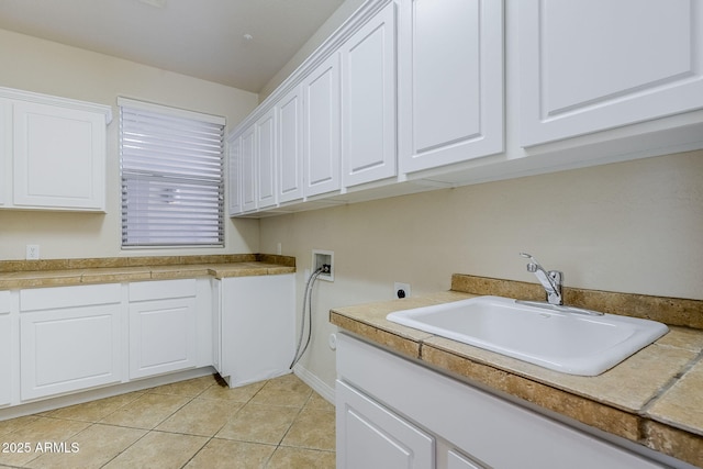 clothes washing area featuring cabinet space, a sink, hookup for a washing machine, electric dryer hookup, and light tile patterned floors