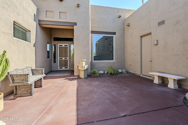 view of exterior entry featuring visible vents, a patio, and stucco siding