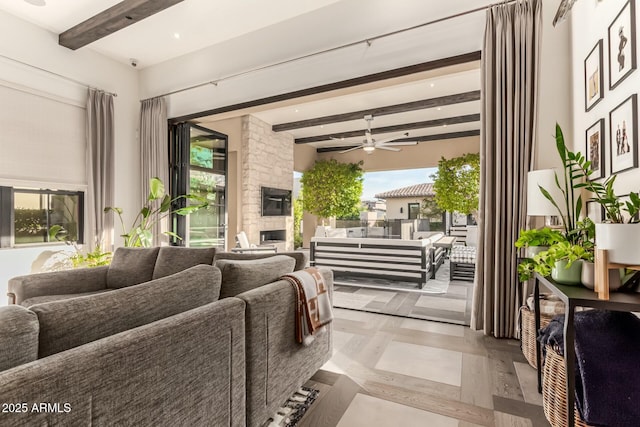 living room with beam ceiling, ceiling fan, a stone fireplace, and a healthy amount of sunlight