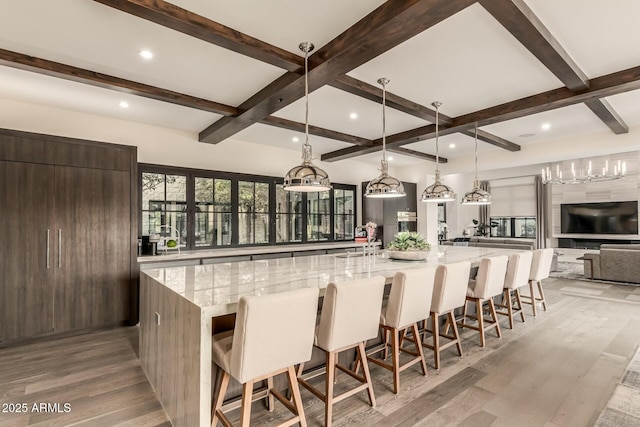 kitchen featuring a spacious island, decorative light fixtures, light stone counters, and light wood-type flooring