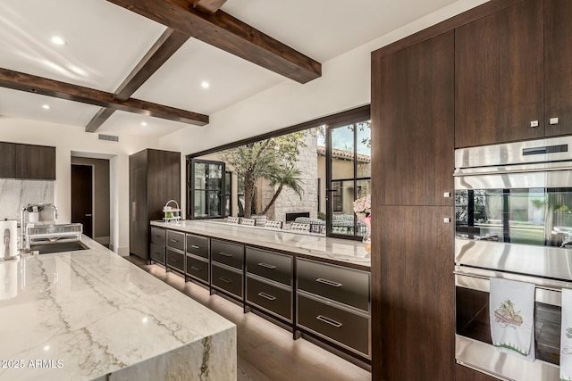 kitchen featuring beamed ceiling, sink, dark brown cabinetry, light stone countertops, and stainless steel double oven