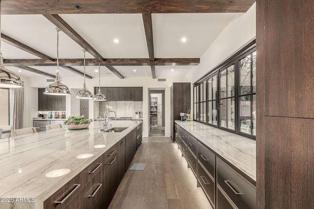 kitchen featuring sink, light stone counters, hanging light fixtures, beamed ceiling, and hardwood / wood-style floors