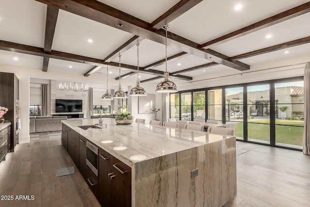 kitchen with decorative light fixtures, sink, a large island, light stone countertops, and light wood-type flooring