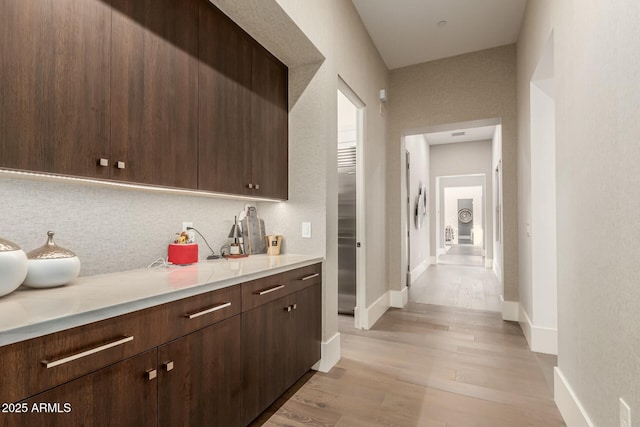 kitchen featuring tasteful backsplash, dark brown cabinets, and light wood-type flooring