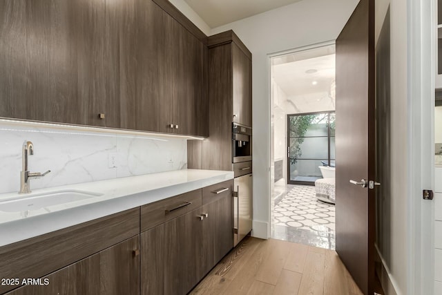 kitchen featuring sink, backsplash, oven, dark brown cabinets, and light wood-type flooring