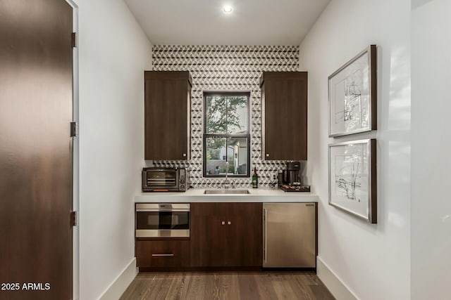 bar with dark wood-type flooring, sink, fridge, wall oven, and decorative backsplash