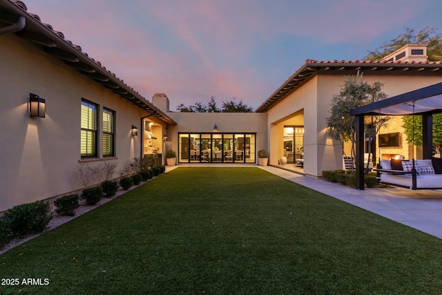 back house at dusk featuring a pergola and a lawn