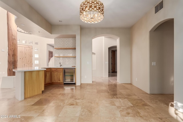 kitchen with pendant lighting, sink, light brown cabinetry, kitchen peninsula, and beverage cooler