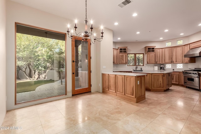 kitchen with wall chimney range hood, high end stove, a chandelier, decorative light fixtures, and a kitchen island