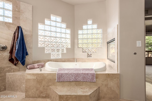 bathroom with tile patterned flooring, tile walls, a wealth of natural light, and tiled tub