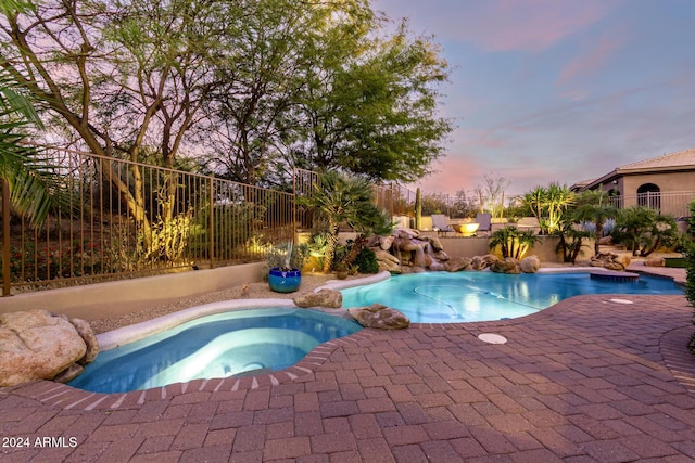 pool at dusk featuring an in ground hot tub and a patio