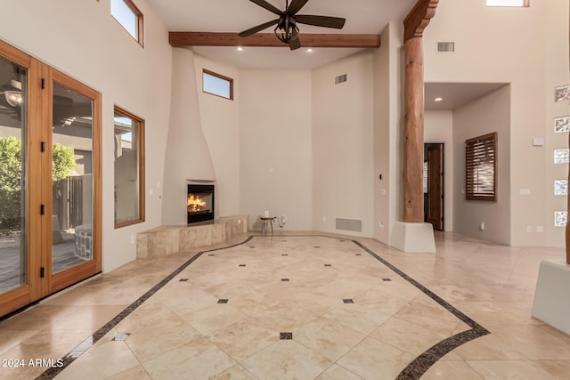 empty room with a large fireplace, ceiling fan, beam ceiling, and a high ceiling