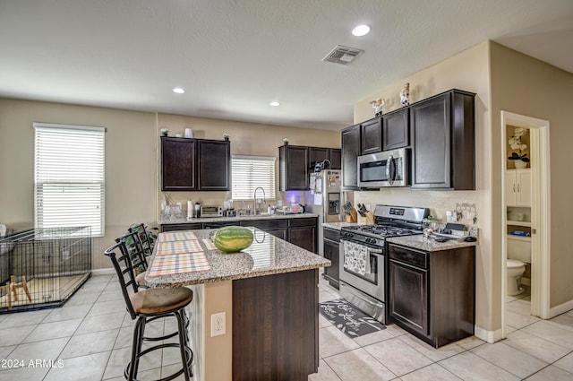 kitchen with visible vents, a kitchen island, dark brown cabinets, appliances with stainless steel finishes, and a kitchen bar