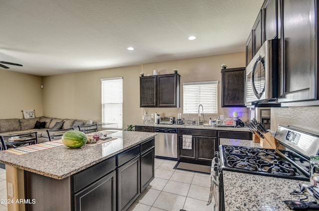 kitchen featuring a sink, a kitchen island, stainless steel appliances, dark brown cabinetry, and light tile patterned flooring