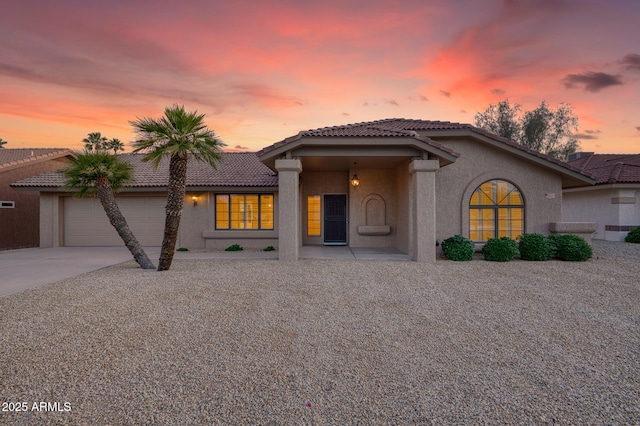 mediterranean / spanish-style house featuring driveway, a tiled roof, stucco siding, and a garage