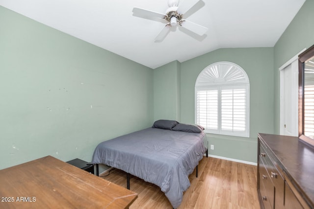 bedroom with baseboards, light wood finished floors, vaulted ceiling, and a ceiling fan