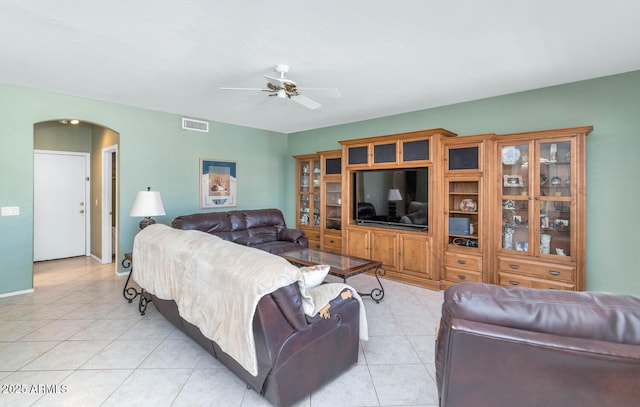 living room featuring ceiling fan, light tile patterned floors, arched walkways, visible vents, and baseboards