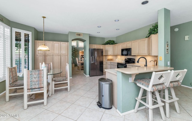 kitchen with light countertops, light brown cabinetry, black appliances, and a wealth of natural light