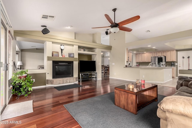 living area featuring wood finished floors, ceiling fan, a glass covered fireplace, and visible vents