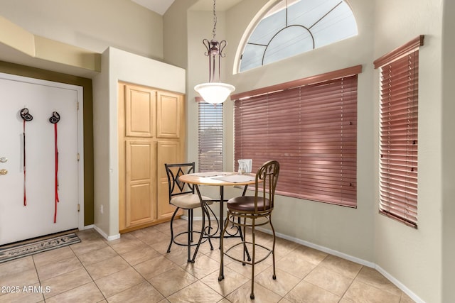 dining space featuring light tile patterned floors, a towering ceiling, and baseboards
