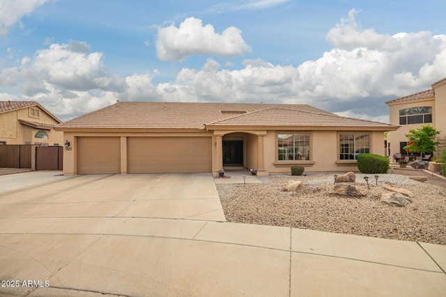 view of front of home featuring stucco siding, driveway, a tile roof, a garage, and fence