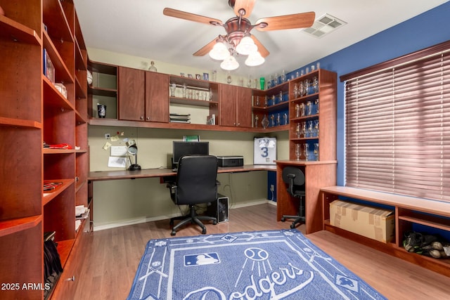 office area featuring baseboards, built in study area, visible vents, ceiling fan, and wood finished floors