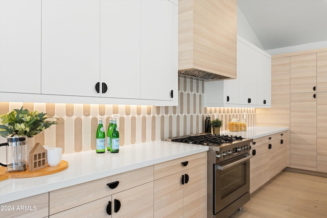 kitchen with premium range hood, high end stainless steel range oven, light hardwood / wood-style floors, decorative backsplash, and white cabinets