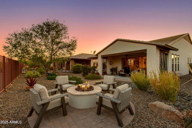 4577 Tenderfoot Way, Wickenburg, AZ 85390 - back of house at dusk with ceiling fan, a patio area, fence, an outdoor fire pit, and stucco siding